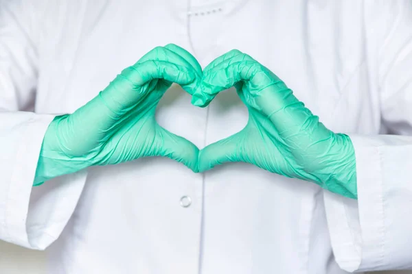 Doctor\'s hands in green medical gloves in the shape of a heart on a background of white medical clothes