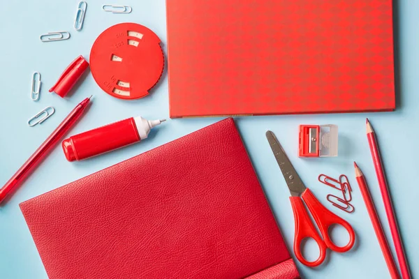 Red stationery: notepads, scissors, pen, pencils, a correction pen, a sharpener, paper clips, and a device for the values of the trigonometric functions of the angles on a blue background