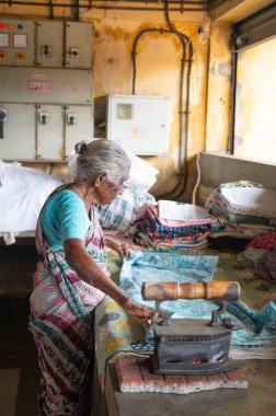 Geleneksel giysili kadın elinde antika bir kömür ütüsüyle, Dhobi Ghat, Kochi, Hindistan 'da açık hava çamaşırları, 20 Mart 202