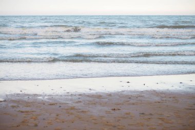 Kum plaj ve gün batımı ile denizde dalgalar.