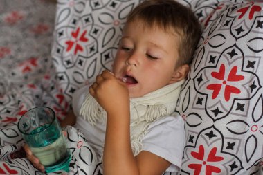 Küçük çocuk atkısı ve elinde su ve uyuşturucuyla yatakta yatıyor.