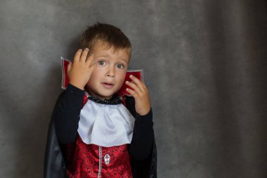 Gri arka planda cadılar bayramı kostümü giymiş vampir çocuk. Duygusallık. 