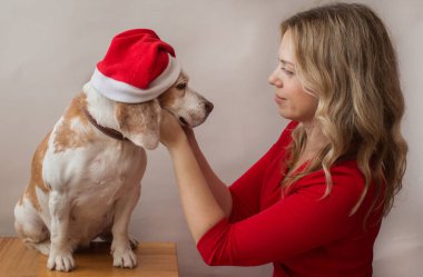 Kırmızı elbiseli kadın içeride Noel Baba şapkalı bir köpek tutuyor. En iyi arkadaşlar kutsasın. 