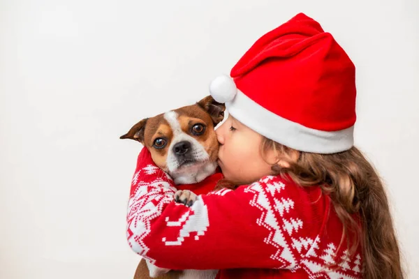 Little girl in Christmas jacket and hat kissing dog