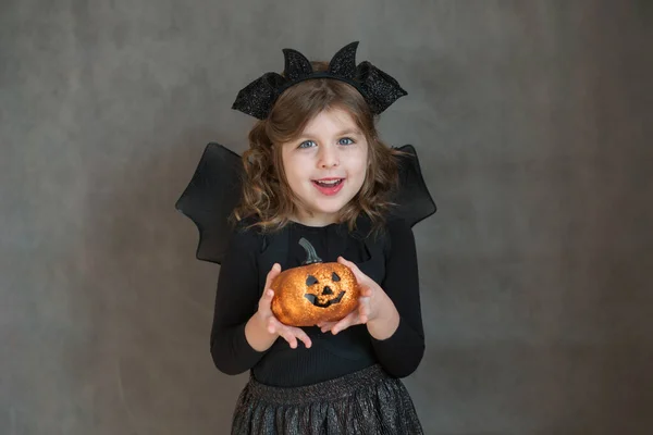 Šťastná dívka v halloween kostým s dýní na šedém pozadí — Stock fotografie