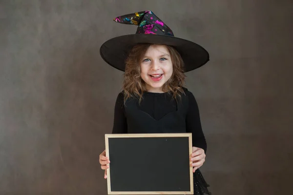 Šťastná dívka v halloween čarodějnice kostým s černým psacím stolem v ruce — Stock fotografie