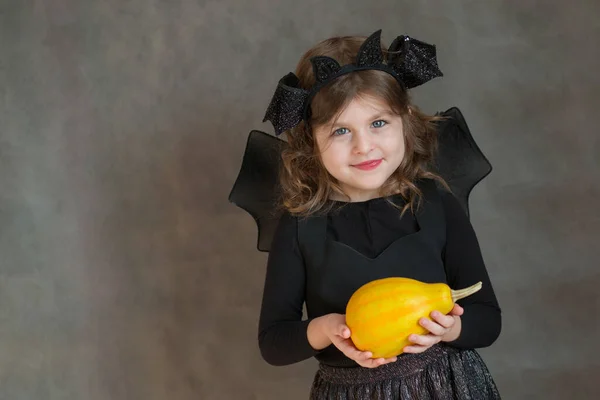 Šťastná dívka v halloween kostým se žlutou malou dýní na šedém pozadí — Stock fotografie