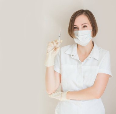 Eldivenli ve maskeli kadın doktor iğne tutuyor.