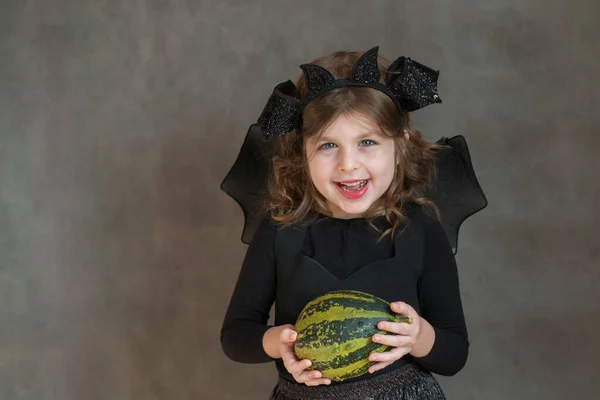 Šťastná dívka v halloween kostým s malou zelenou dýně na šedém pozadí — Stock fotografie