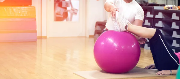 exercising with personal trainer on large stability ball in studio fitness back physiotherapy