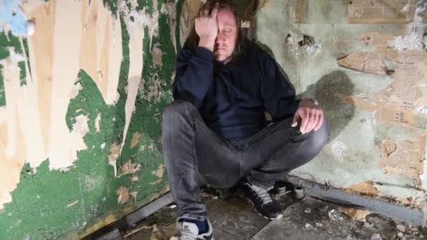 Depressed and angry man is sitting in the corner in an abandoned house — Stock Video