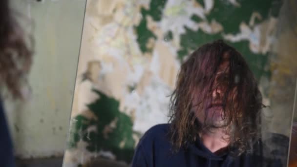 Homem deprimido e louco senta-se em um sofá em uma casa abandonada e olha em um espelho — Vídeo de Stock