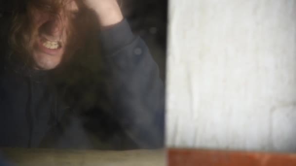 Depressed and angry man is sitting in front of his reflection in an old abandoned house — Stock Video