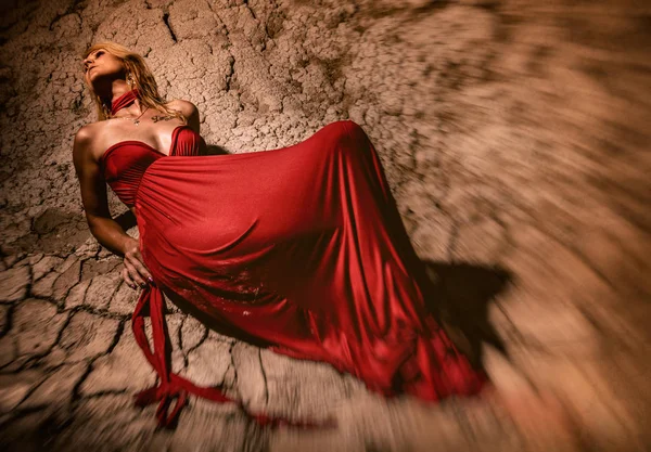 Elegancia sexy dama en vestido rojo se encuentra en el suelo seco desierto — Foto de Stock