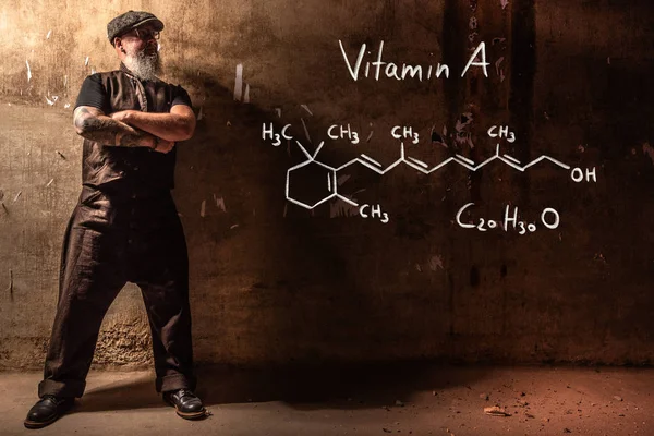 Bärtiger alter Mann präsentiert handgezeichnete chemische Formel von Vitamin A — Stockfoto