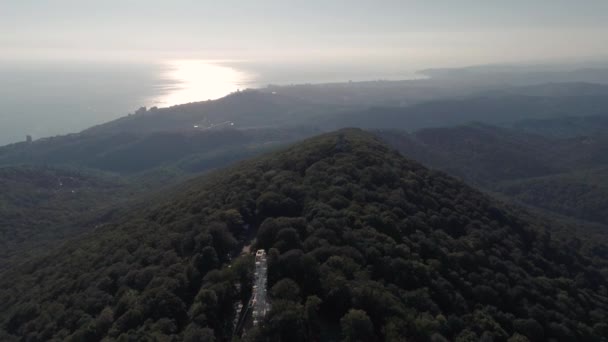 Voo de helicóptero sobre a floresta verde e montanhas. Mar e praia no horizonte. Sol ao pôr-do-sol. Relaxamento e solidão na viagem. Sochi Akhun Mountain. Inquérito aéreo . — Vídeo de Stock