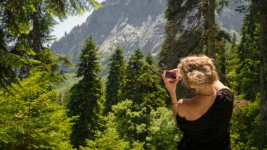 Güneşli bir günde, güzel bir turist kızın portresi, bir sırt çantasıyla, moda bir kadınla, ağaçların arka planında, ormanda yürüyor. Konsept: eğlence, güzel manzara, spor, seyahat.