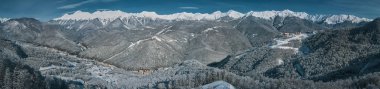 Panorama of the mountains in the snow. Gray sky over mountains. Vacation in Sochi, rest in the mountains. Skiing, snowboarding, freeride. Aerial photography with copter. Mountain road clipart