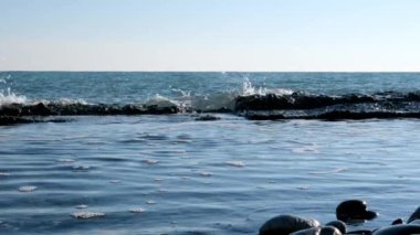 Deniz dalgalarının yavaş çekim hareketi. Skyline. Mavi gökyüzü ve su. Sakin bir deniz var. Kıyıda dalgalar kırılıyor.