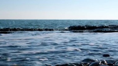 Deniz dalgalarının yavaş çekim hareketi. Skyline. Mavi gökyüzü ve su. Sakin bir deniz var. Kıyıda dalgalar kırılıyor.