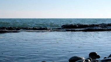 Deniz dalgalarının yavaş çekim hareketi. Skyline. Mavi gökyüzü ve su. Sakin bir deniz var. Kıyıda dalgalar kırılıyor.