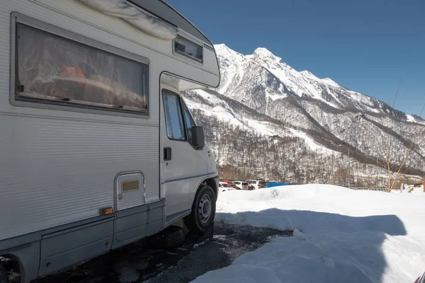 Camper araba karla kaplı dağlara karşı otoparkta duruyor. Kayak merkezi Rosa Khutor Sochi. Dağlarda açık hava eğlencesi. Yolda hayat. Van turizmi.