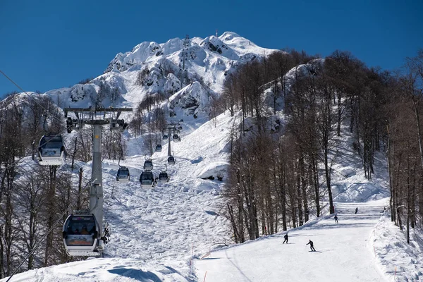 Teleférico en las montañas de Krasnaya Polyana Sochi en el que los esquiadores y snowboarders suben a la cima de la montaña Aibga. Bajando de la montaña. Estación de esquí Rosa Khutor . — Foto de Stock
