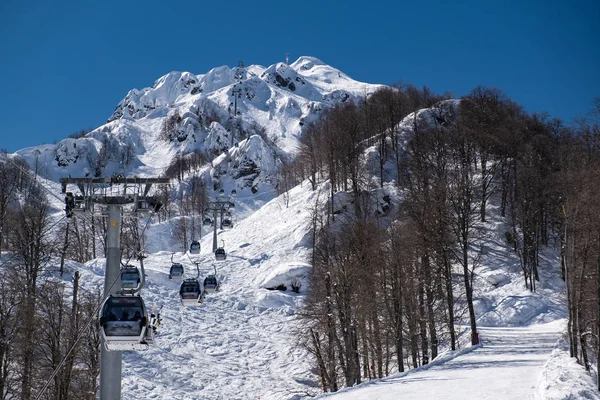 Teleférico en las montañas de Krasnaya Polyana Sochi en el que los esquiadores y snowboarders suben a la cima de la montaña Aibga. Bajando de la montaña. Estación de esquí Rosa Khutor . — Foto de Stock