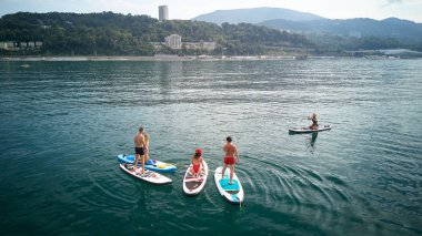 Hava fotoğrafçılığı. Yukarıdan manzara. Mayo giyen beş gençten oluşan bir şirket yoga yapıyor ve Karadeniz,Soçi'de Sup sörfü yaparken fotoğraflandı. Su üzerinde aktif dinlenme.
