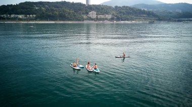 Hava fotoğrafçılığı. Yukarıdan manzara. Mayo giyen beş gençten oluşan bir şirket yoga yapıyor ve Karadeniz,Soçi'de Sup sörfü yaparken fotoğraflandı. Su üzerinde aktif dinlenme.