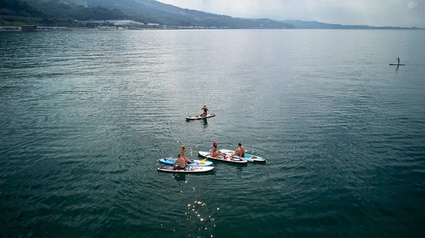 Hava fotoğrafçılığı. Yukarıdan manzara. Mayo giyen beş gençten oluşan bir şirket yoga yapıyor ve Karadeniz,Soçi'de Sup sörfü yaparken fotoğraflandı. Su üzerinde aktif dinlenme.