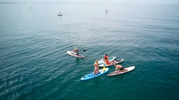 Fotografia aérea. A vista de cima. Uma empresa de cinco jovens em trajes de banho fazendo ioga e fotografado em SUP surf no mar negro, Sochi. Descanso ativo na água . — Fotografia de Stock