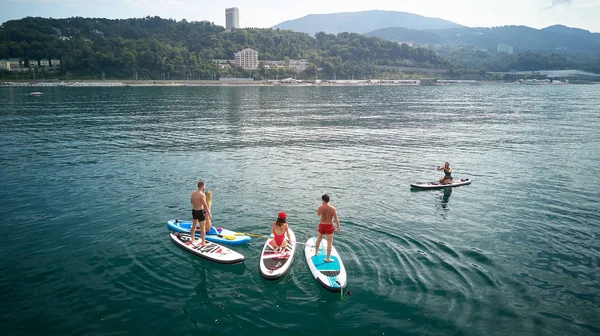 Hava fotoğrafçılığı. Yukarıdan manzara. Mayo giyen beş gençten oluşan bir şirket yoga yapıyor ve Karadeniz,Soçi'de Sup sörfü yaparken fotoğraflandı. Su üzerinde aktif dinlenme.