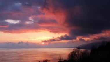 Denizüzerinde kırmızı gün batımı. Güneş ufukta batıyor. Dağların ve denizin akşam manzarası. Gökyüzünde büyük Cumulus bulutları. Yukarıdan güzel manzara.