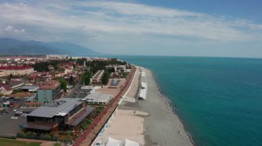 Havadan video çekimi. Imeretinsky tatil beldesinin panoramik manzarası. Soçi'de Karadeniz. Temiz ve konforlu plaj. Rekreasyon alanı. Kafkas dağı. Yukarıdan manzara. Turizm sezonu. Lüks otel.
