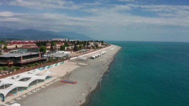 Havadan video çekimi. Imeretinsky tatil beldesinin panoramik manzarası. Soçi'de Karadeniz. Temiz ve konforlu plaj. Rekreasyon alanı. Kafkas dağı. Yukarıdan manzara. Turizm sezonu. Lüks otel.