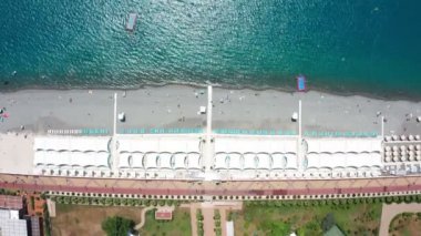 Havadan video çekimi. Kıyı şeridi. Rekreasyon ve yüzme alanı. Soçi 'de Karadeniz 'de donatılmış plaj, Rusya. Tatil sezonu. Kamera görünümü aşağı. Mavi deniz suyu. Kıyı boyunca uçan.