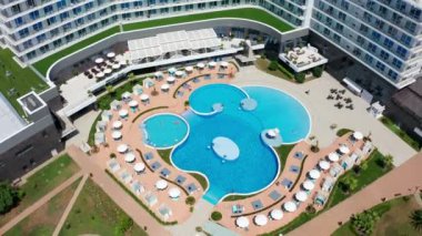 Havadan video çekimi. Tesis bünyesinde açık mavi su içeren Yüzme Havuzu. Tesiste erkekler ve kadınlar dinlenebilirler. Dairesel Panorama. Güneşli gün.
