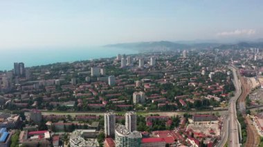 Havadan video çekimi. Kentsel altyapı. Yukarıdan manzara. Şehrin yerleşim alanları. Deniz manzarası. Güneşli bir yaz günü. Otoyol. Rusya'nın Karadeniz kıyıları, Soçi şehri.