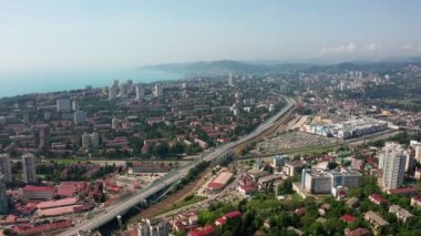 Havadan video çekimi. Kentsel altyapı. Yukarıdan manzara. Şehrin yerleşim alanları. Deniz manzarası. Güneşli bir yaz günü. Otoyol. Rusya'nın Karadeniz kıyıları, Soçi şehri.