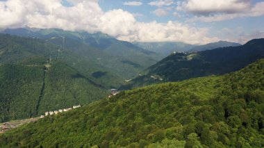 Havadan video çekimi. En yüksek dağ. Yeşil orman. Kayak merkezi Rosa Khutor. Krasnaya Polyana, Soçi. Gökyüzündeki bulutlar. Açık hava eğlencesi. Otel dağlarda. Teleferik.