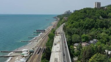 Deniz kıyısındaki yol. Okyanus kıyısında. Devam edelim. Otoyol. Yukarıdan bak. Hava videosu. Yeşil ağaçlar. Açık mavi gökyüzü. Kumsal. Soçi. Rusya