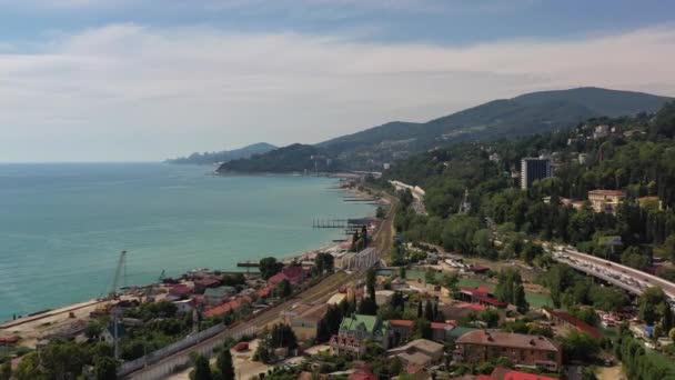 Στο Cityscape. Θέα από ψηλά. Ωκεανίδα. Σότσι. Ρωσία. Σάμερ. Εναέρια βίντεο. Παραλία. Η Μαύρη Θάλασσα. Ο δρόμος κατά μήκος της θάλασσας. Ψηλά βουνά. Καθαρός καιρός. Μετακίνηση της κάμερας — Αρχείο Βίντεο