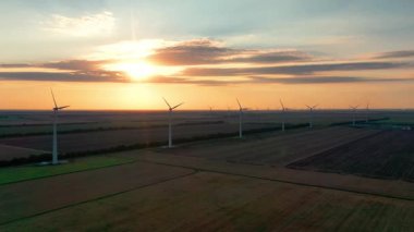 Geniş rüzgar türbinleri. Saha havası manzaralı parlak turuncu günbatımı. Rüzgâr parkı yavaş çekim drone dönüşü. Siluetler yel değirmenleri. Alternatif enerji. Rüzgar türbinlerinin hava görüntüsü Enerji Üretimi 