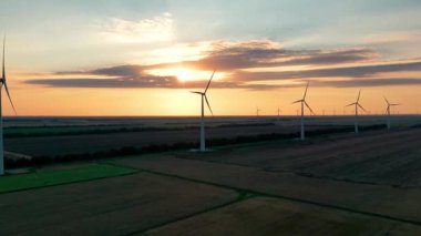Geniş rüzgar türbinleri. Saha havası manzaralı parlak turuncu günbatımı. Rüzgâr parkı yavaş çekim drone dönüşü. Siluetler yel değirmenleri. Alternatif enerji. Rüzgar türbinlerinin hava görüntüsü Enerji Üretimi 