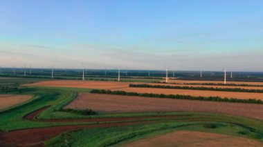 Geniş rüzgar türbinleri ve saha manzarası günbatımında bıçaklar. Rüzgar parkı drone dönüşü. Siluetler yel değirmenleri. Alternatif enerji. Rüzgar türbinlerinin hava görüntüsü Enerji Üretimi. Gün doğumunda türbinler
