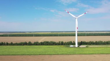 Elektrik üreten rüzgar türbinleri. Rüzgâr değirmeni güç teknolojisi. Enerji Üretiminde hava aracı görüntüsü. Rüzgâr türbinleri çiçek açan bir arazide duruyor. yeşil alan. 