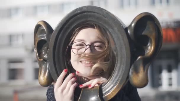 Jeune fille en lunettes posant avec une sculpture en forme d'oreilles pour la photographie — Video