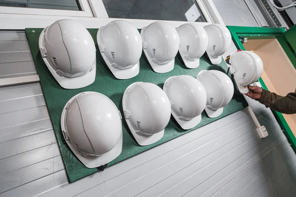 Male hand of worker takes hard hat in factory. Construction safety helmets hanging on wall. Safety concern for engineering or building work site. Wearing helmet can safe contractor life in plant