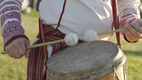 Man in traditional russian clothes dancing and playing on folklore drum outdoor. Man wearing national Finno-Ugric clothes.